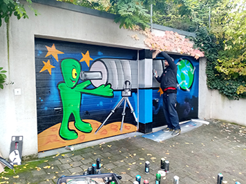 painting on a garage door of an alien looking through a telescope at Earth.