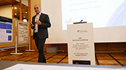 Male speaker in front of large screen with posters on the left