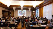 View of the audience, speaker and large screen from the back of the room